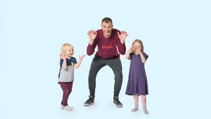 En vuxen och två små barn står tillsammans i lekrörelser och ser glada ut.
