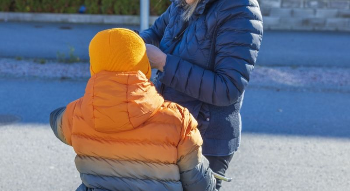 Vuxen hjälper barn i orangea jacka