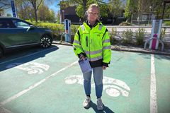 Person i lysande gul jacka står på en parkeringsplats för elbilar.