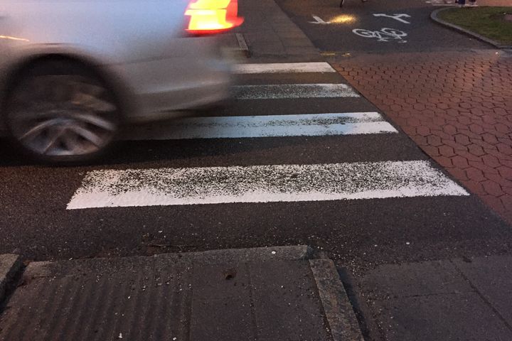 En bil kör över slitna vägmarkeringar i mörker.