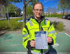 Kvinna i gul reflexjacka håller i ett häfte.