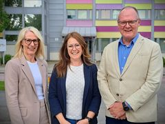 Tre personer står utomhus framför en byggnad.