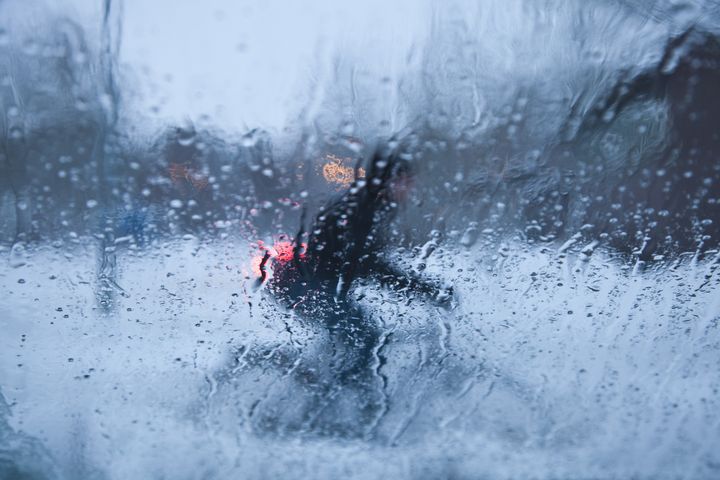 En person cyklar i regnet, sedd genom ett vattendränkt fönster.