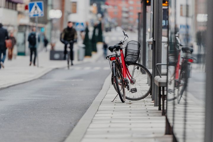 En röd cykel parkerad vid en busshållplats i stadslandskap.