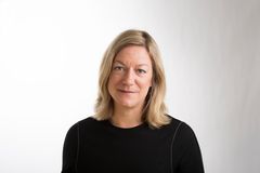 Kvinna med blont hår som bär en svart tröja, mot en vit bakgrund.