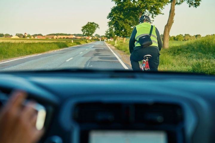 En person cyklar på en landsväg, sedd från en bil som kör bakom.