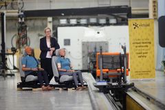 En person står bredvid två krockdockor som sitter i bilsäten i en testanläggning.