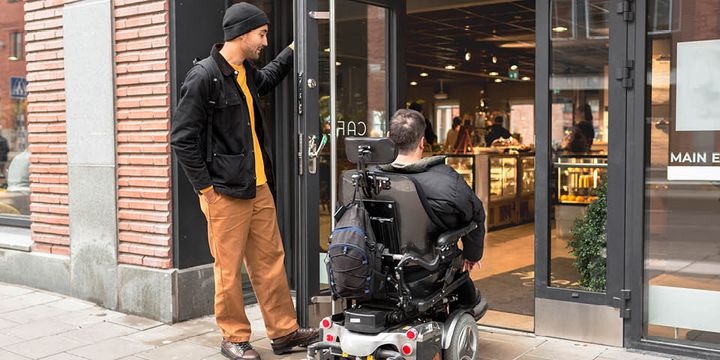 Två personer varav en i rullstol är påväg in genom en dörr.