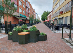 En folktom gågata med uteserveringar och blomsterarrangemang med sittplatser.