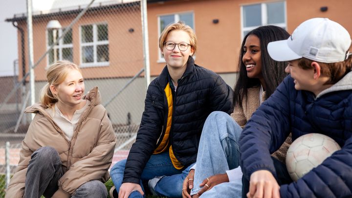 Fyra ungdomar sitter på en trappa på en skolgård och pratar glatt med varandra.