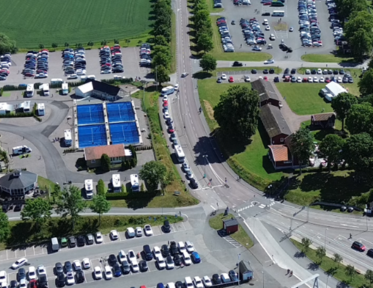 Dr%F6narbild%20%F6ver%20stora%20fullbelagda%20parkeringsytor%20och%20en%20gata%20med%20bilar%20i%20k%F6.