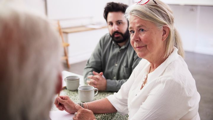 Tre personer samtalar vid ett bord med kaffekoppar.