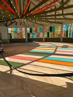 Insidan av en byggnad med dansgolv, ljusinsläpp och fönsterpartier i olika färger.