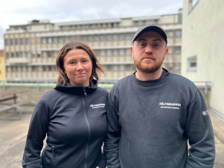 Två personer står framför en byggnad.