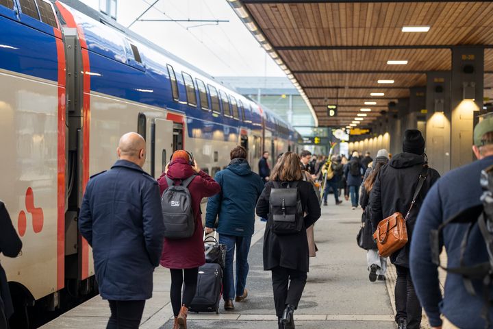 Många människor som går på perrong intill ett blåvitt tåg.