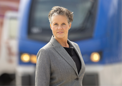 Porträtt på kvinna i gråkavaj framför ett blått Mälartåg.