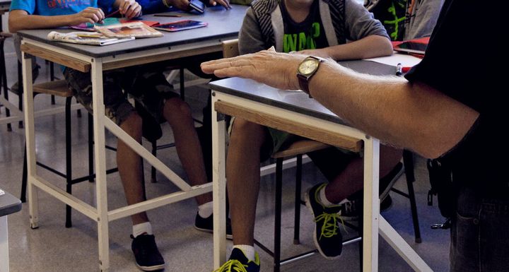 En person sitter framför ett klassrum med elever som sitter vid sina bänkar.