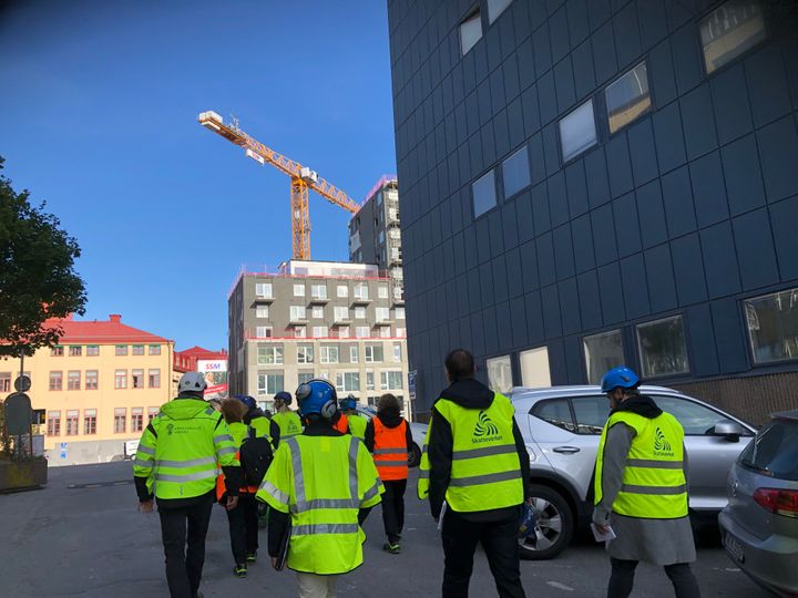 Ryggar på en grupp arbetsplatskontrollanter från olika myndigheter som inspekterar en byggarbetsplats.