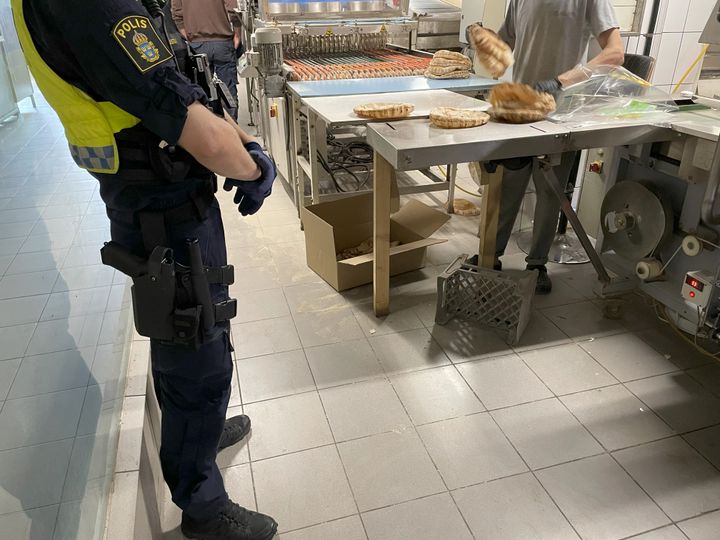 En polisman står framför en brödmaskin där en arbetstagare står och arbetar.