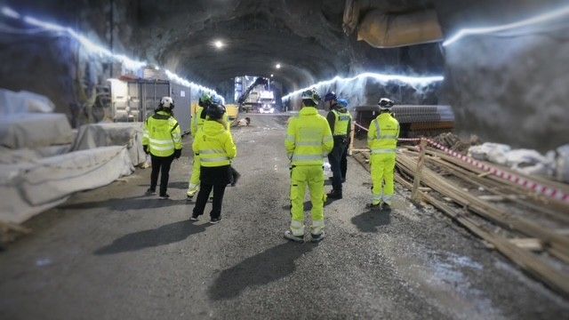 Personer i reflexkläder står i en osläckt tunnel med arbetsmaterial runt omkring.