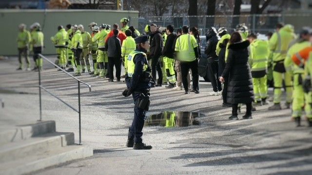 Polis och personer i arbetskläder samlade utomhus.