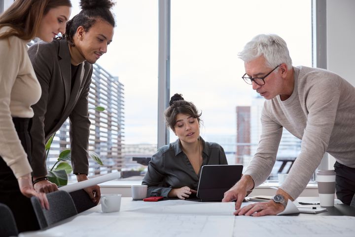 Fyra personer diskuterar över dokument på ett bord i ett kontor.