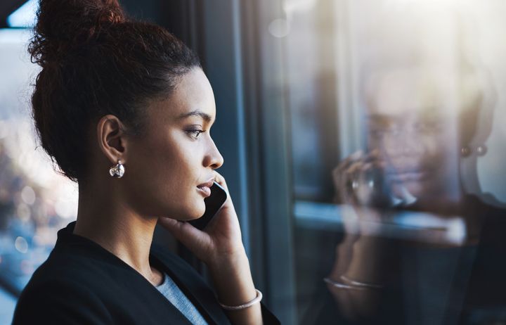 Kvinna i profil pratar i mobiltelefon och tittar ut genom ett fönster.