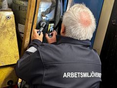 Person i Arbetsmiljöverkets jacka använder en kamera för inspektion.
