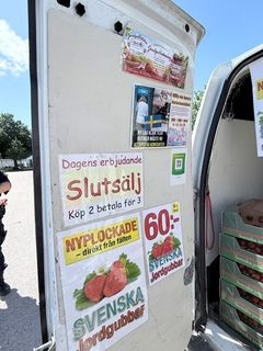 En skåpbil med skyltar som annonserar erbjudanden för svenska jordgubbar och information om priser.
