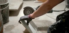 En person skär en kakelplatta med en vinkelslip i byggmiljö.