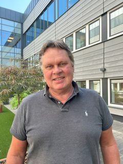 Projektledare Magnus Henriksson, klädd i grå pikétröja, står utomhus framför en modern byggnad.