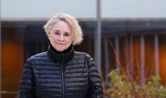 Person i svart jacka, står framför en byggnad.