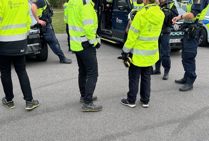 Poliser och arbetsmiljöinspektörer i gula reflexjackor vid en polisbil.