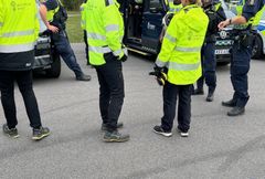 Flera poliser och arbetsmiljöinspektörer i gula reflexjackor står vid en polisbil.