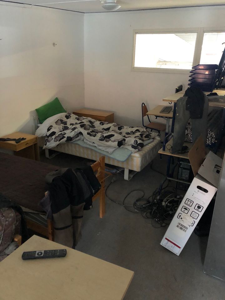 Boende på jobbet med säng, skrivbord, datorutrustning och sladdar på golvet.