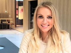 Porträtt av Lana Tomic Lindberg, blond kvinna i vit kavaj, leende mot kameran inomhus.