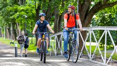 Man och pojke cyklar på bro. Två barn går i bakgrunden. Foto.