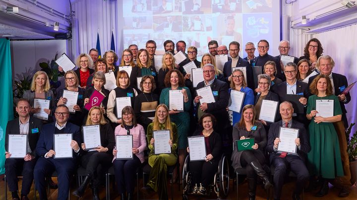 Foto på flera personer som står/sitter med ett varsitt klimatkontrakt. I bakgrunden syns fler personer som medverkar digitalt.