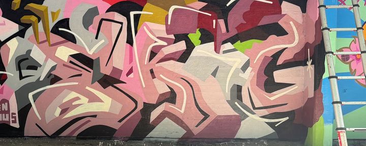 Abstrakt graffitimålning i rosa, bruna och gröna nyanser.