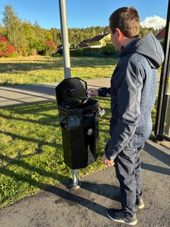 En ung man slänger skräp i en papperskorg med lock. I locket sitter en svart liten låda om innehåller en sensor.