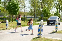 Två skolabarn som springer över bilvägen och en bil som närmar sig.