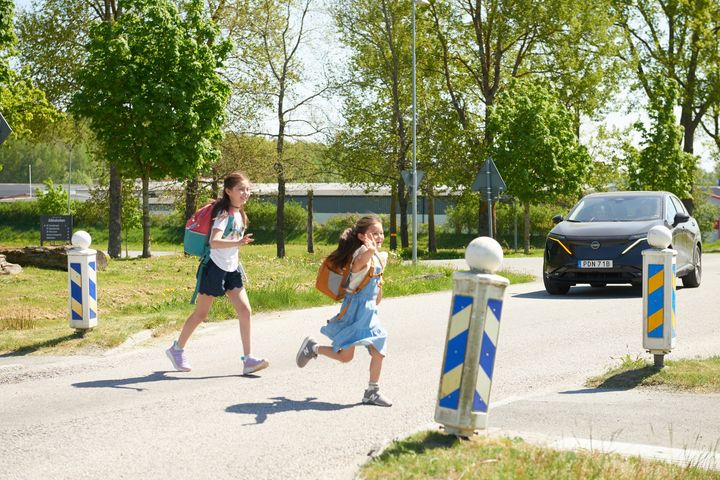 Två skolabarn som springer över bilvägen och en bil som närmar sig.