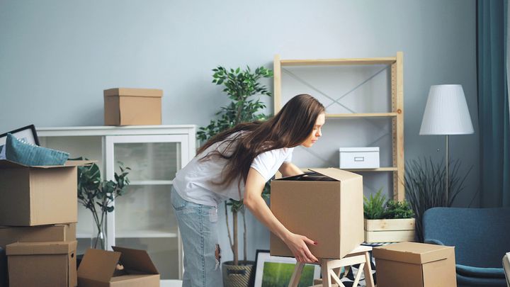 Ung kvinna bär flyttlådor i lägenhet.