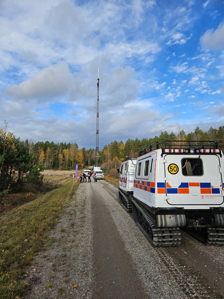 Telemast på en skogsväg med en bandvagn i förgrunden.