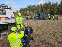 En grupp personer i reflexkläder arbetar med utrustning nära flera fordon på ett fält.