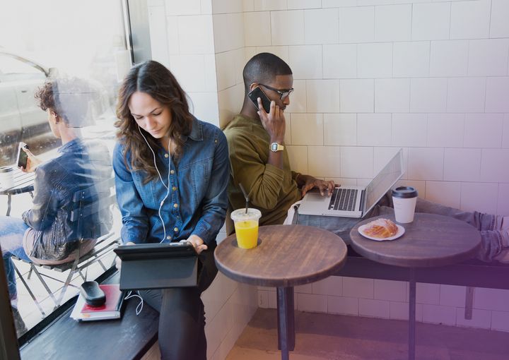 Två personer i cafémiljö med dator och telefon.