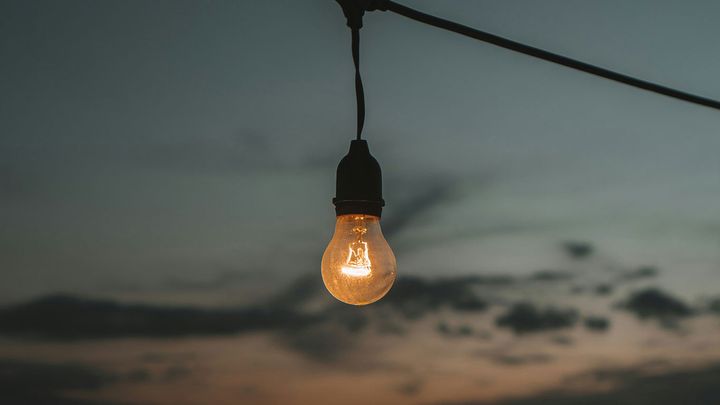 En glödlampa hänger mot en kvällshimmel.