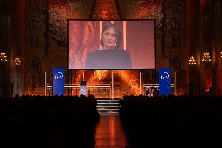 En ceremoni med en person som talar på scenen i ett stort rum, med publik och dekorationer.