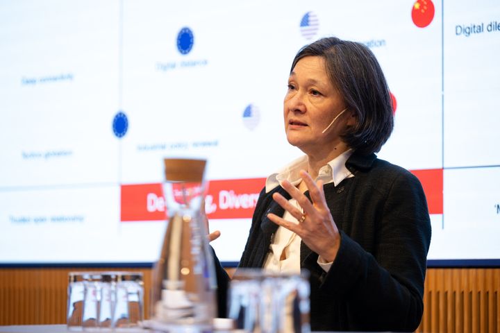 Bild av en Sylvia Schwaag Serger som håller ett föredrag vid ett podium, framför en projicerad presentation.