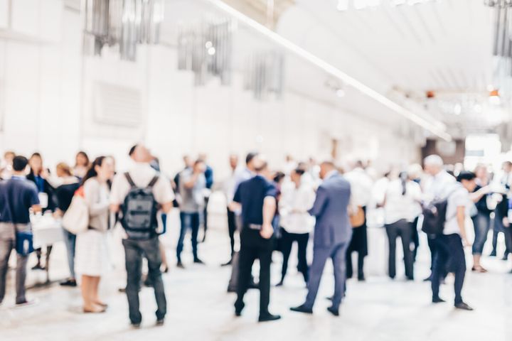 En suddig bild av en grupp människor som minglar inomhus.